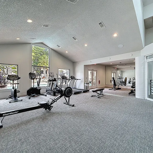 Spacious Gym Interior A spacious interior of a gym featuring various exercise equipment including treadmills, stationary bikes, and weight benches, with large windows allowing natural light to fill the room.