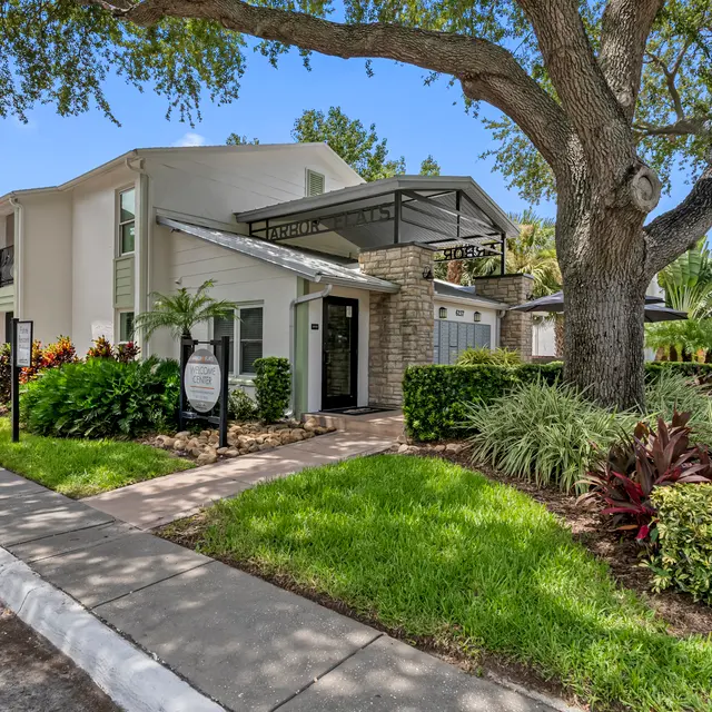 Exterior view of a landscaped apartment complex with a pathway, greenery, and palm trees under a clear blue sky.