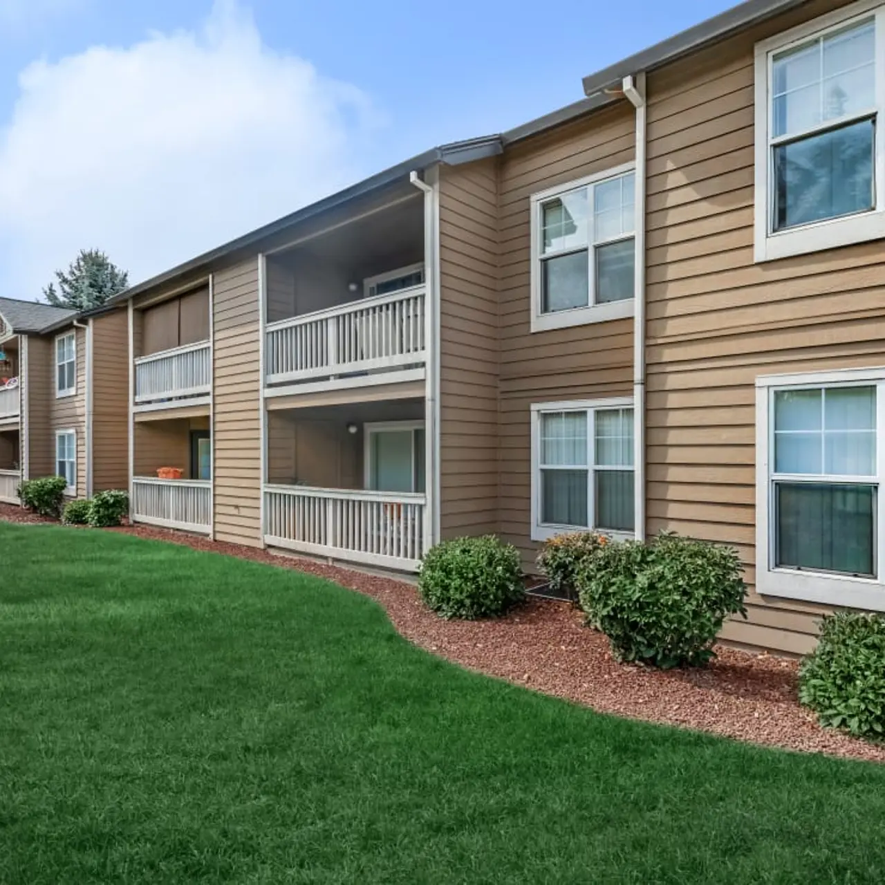 Exterior view of a two-story apartment building surrounded by green grass and landscaped shrubbery.