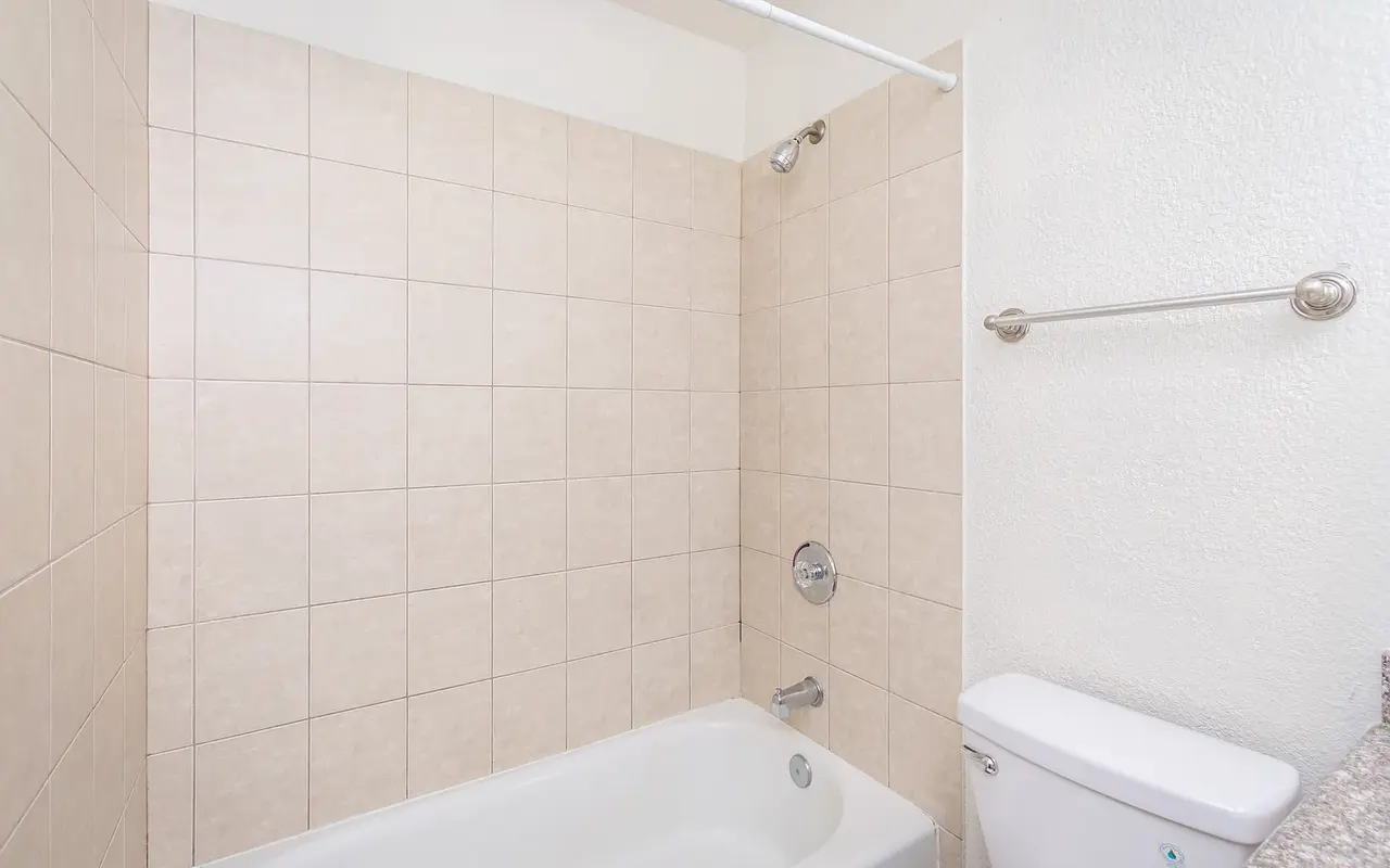 A clean and simple bathroom featuring a bathtub with a showerhead, beige tiled walls, and a white toilet.