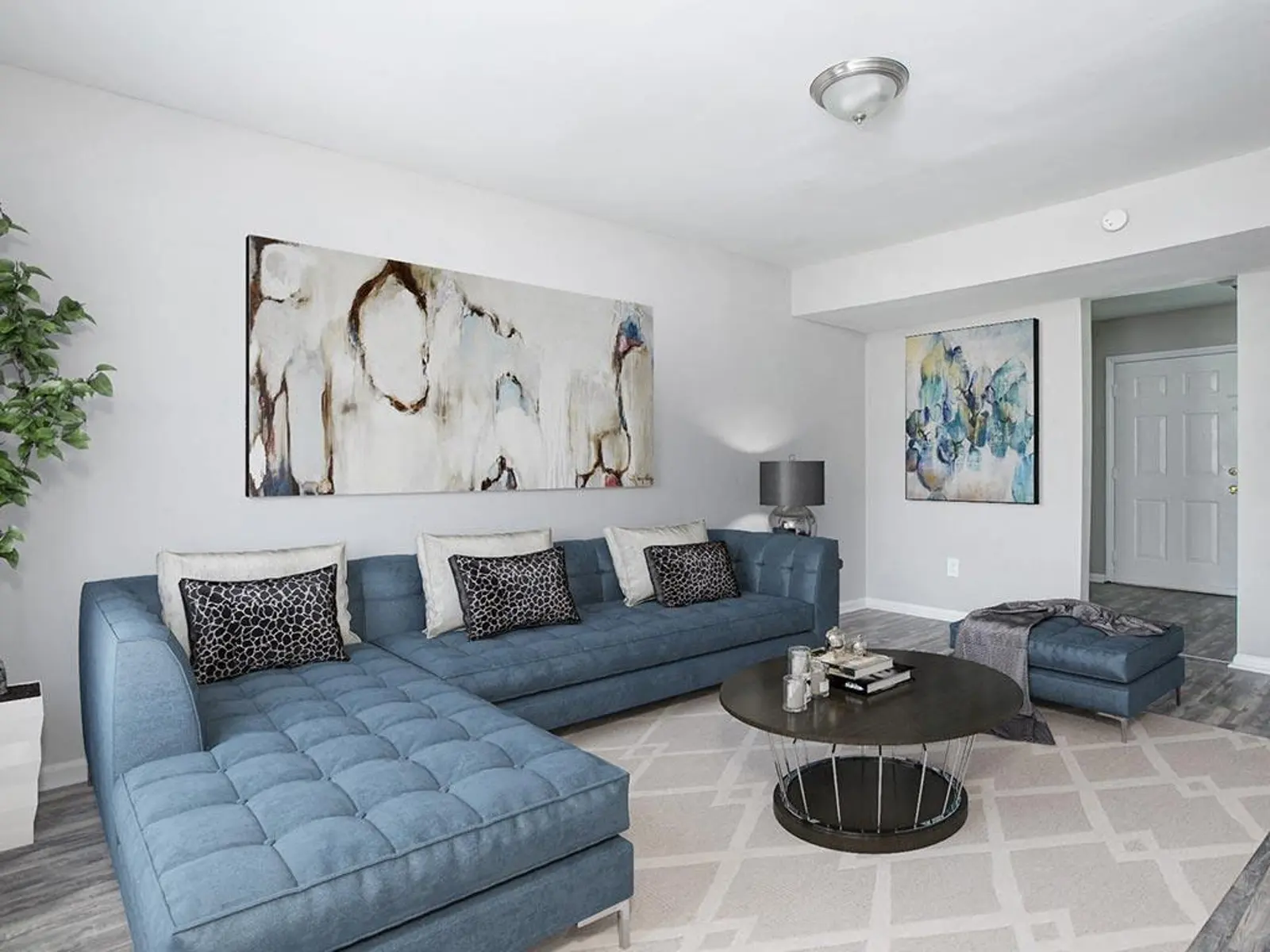 A modern living room with a blue sectional sofa, two abstract paintings on the wall, a round coffee table, and a decorative plant.