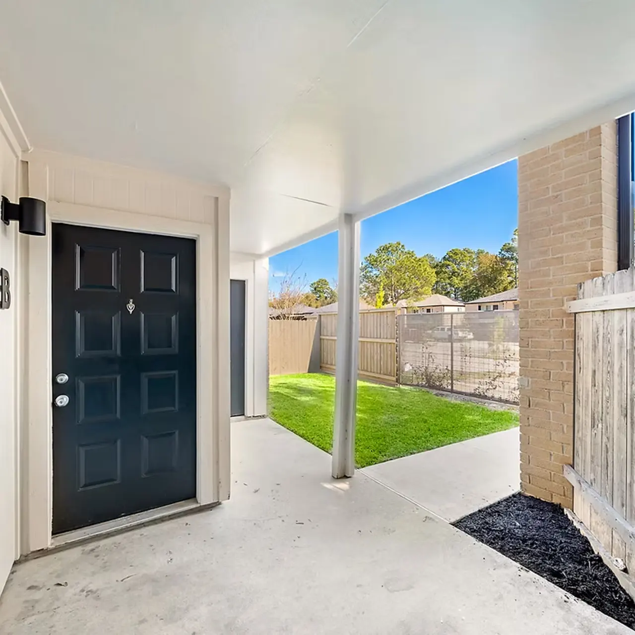A covered entryway leading to a black front door, with a grassy area and fenced courtyard visible on the side.