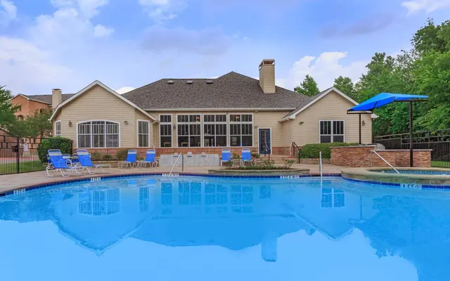 A serene swimming pool area with blue water and lounge chairs, featuring a house in the background.
