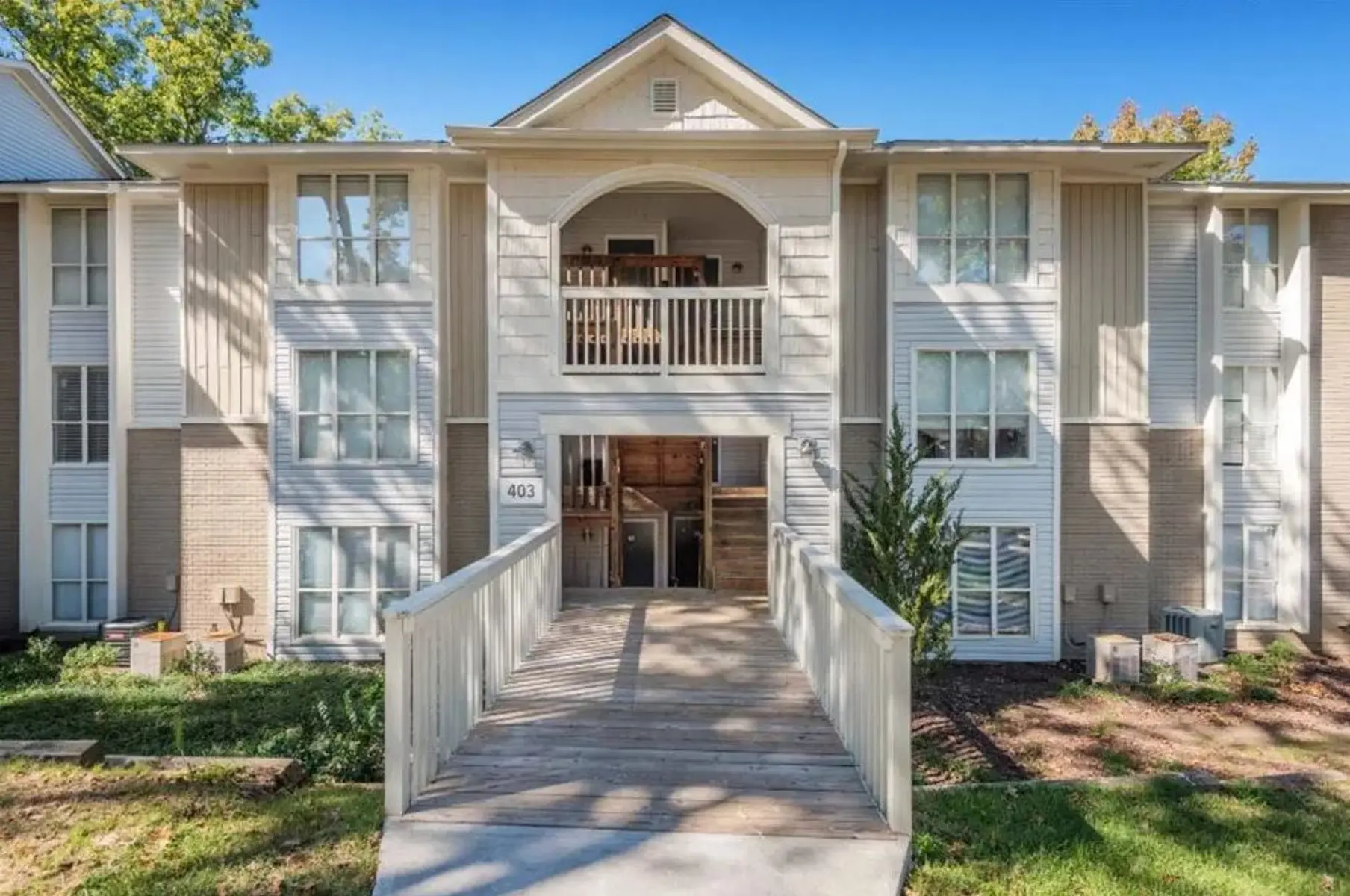 Exterior view of an apartment complex with a wooden walkway leading to the entrance.