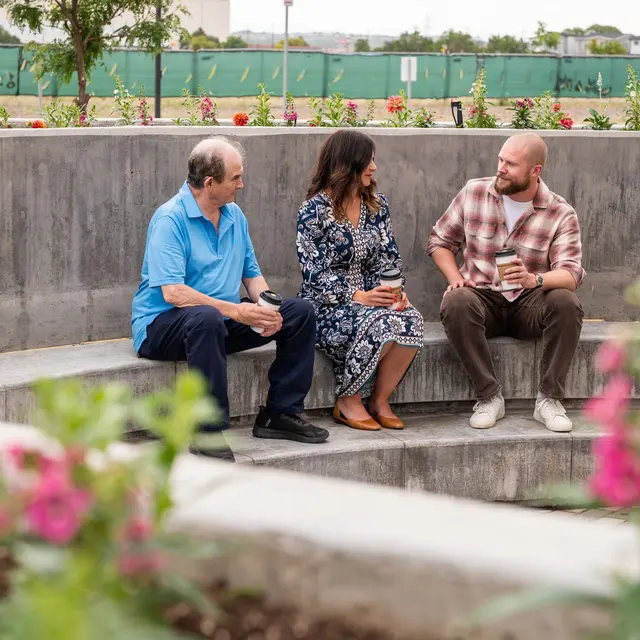 Outdoor Community Gathering Three adults sitting in a circular seating area in a garden, engaged in conversation while holding drinks.