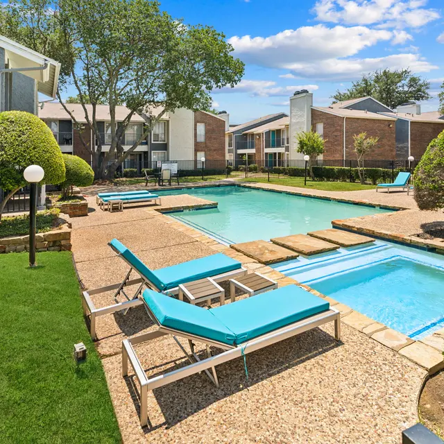 Swimming pool area in an apartment complex with lounge chairs and landscaping.