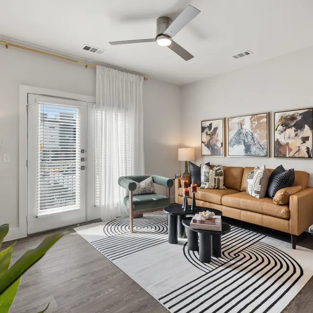 Stylish Modern Living Room A modern living room featuring a brown leather sofa, a green armchair, a patterned area rug, and large windows with natural light. Decorative art pieces adorn the walls, and potted plants add a touch of greenery.