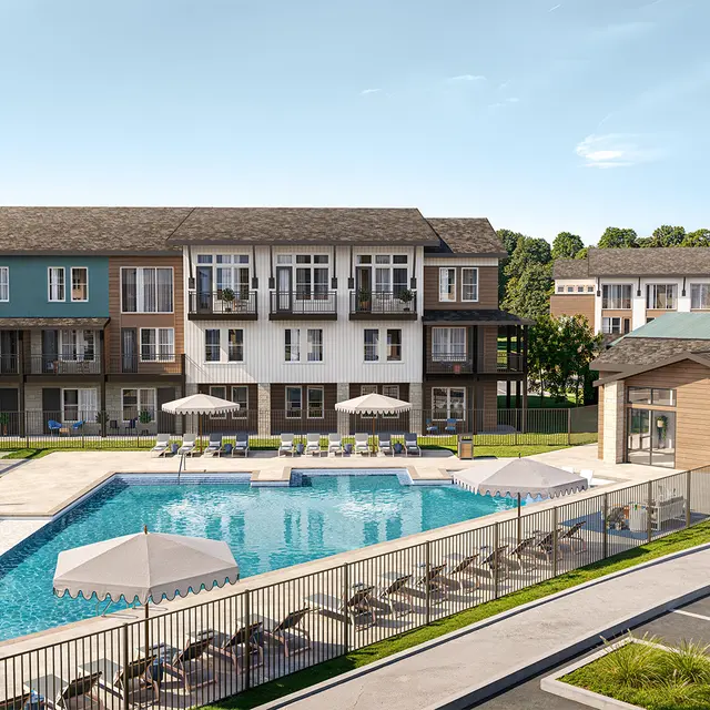 A modern apartment complex featuring a swimming pool surrounded by lounge chairs and umbrellas, with landscaped areas and parking in the foreground.