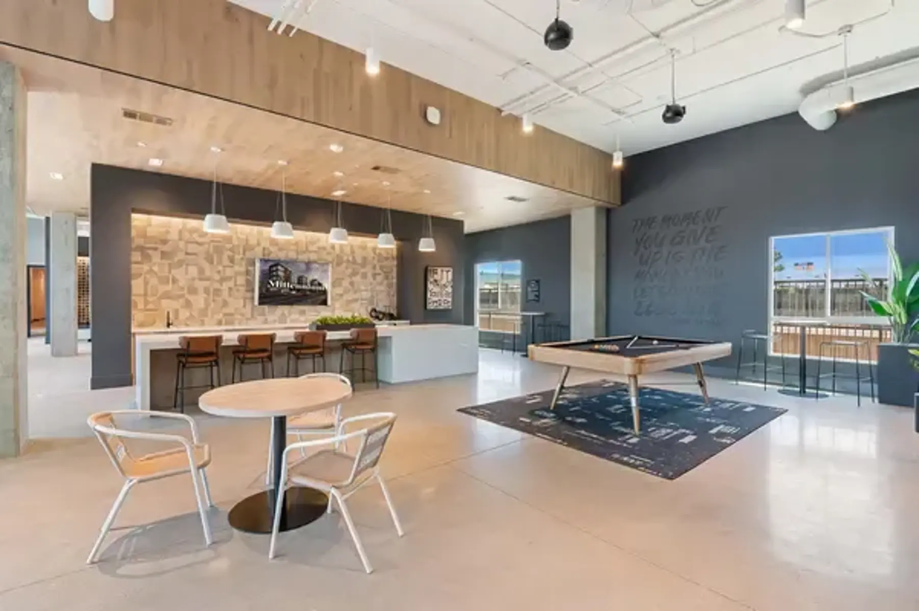 Modern Lounge Area A spacious modern lounge area featuring a bar-style counter with stools, a pool table, and comfortable seating arrangements. Large windows allow natural light to flood in, creating an inviting atmosphere.