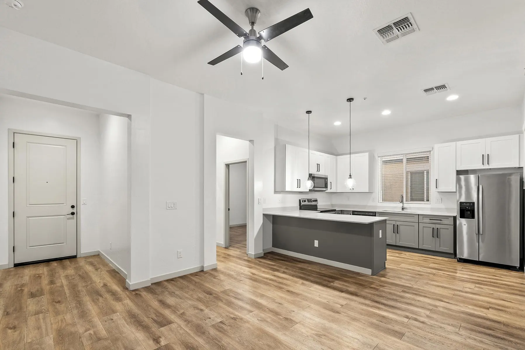 Modern kitchen and living area with wood flooring, stainless steel appliances, and a ceiling fan. Bright and airy layout.
