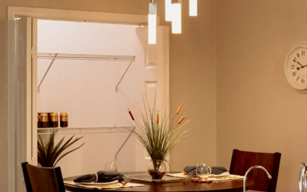 Modern Kitchen Dining Area A modern kitchen dining area with a round table, two chairs, and stylish hanging lights. A plant is in the center of the table, and a pantry door is visible in the background.