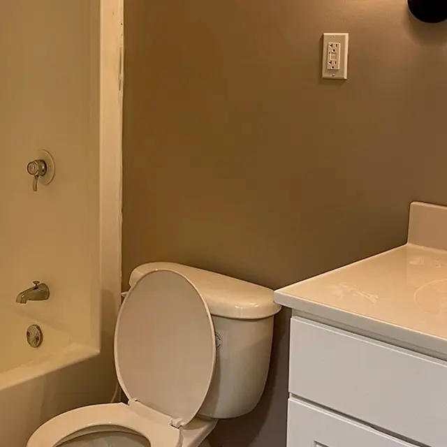 A modern bathroom featuring a white toilet, a sink with a countertop, and a bathtub with a shower. The walls are painted a neutral color, and there is a round mirror on the wall.
