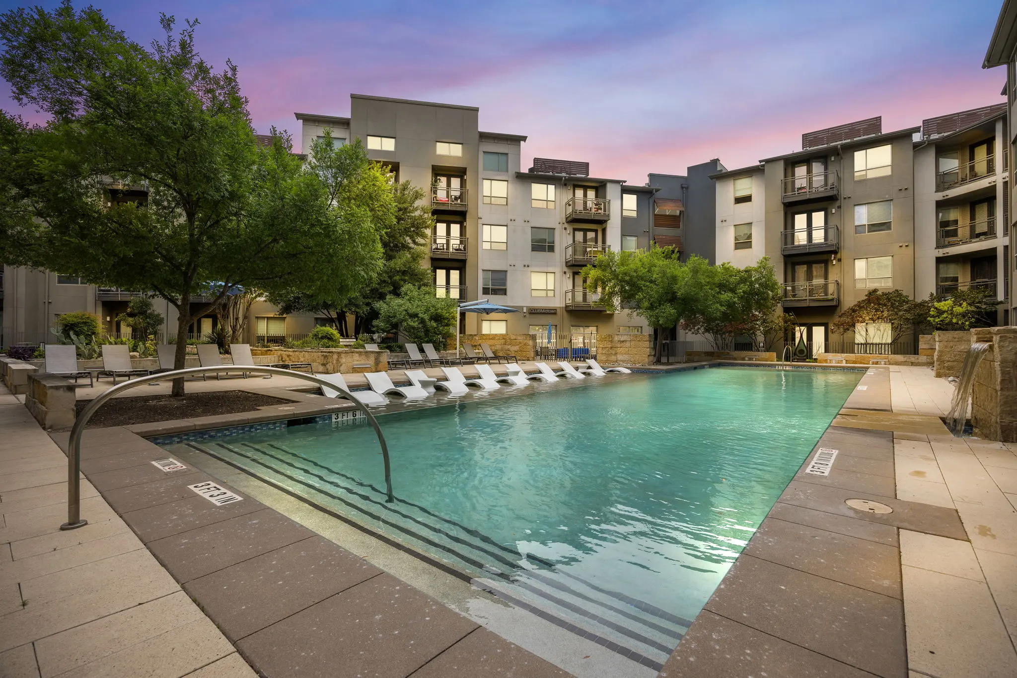 Apartment Complex Pool Area A well-maintained outdoor pool area surrounded by apartment buildings and trees, with lounge chairs along the pool's edge.