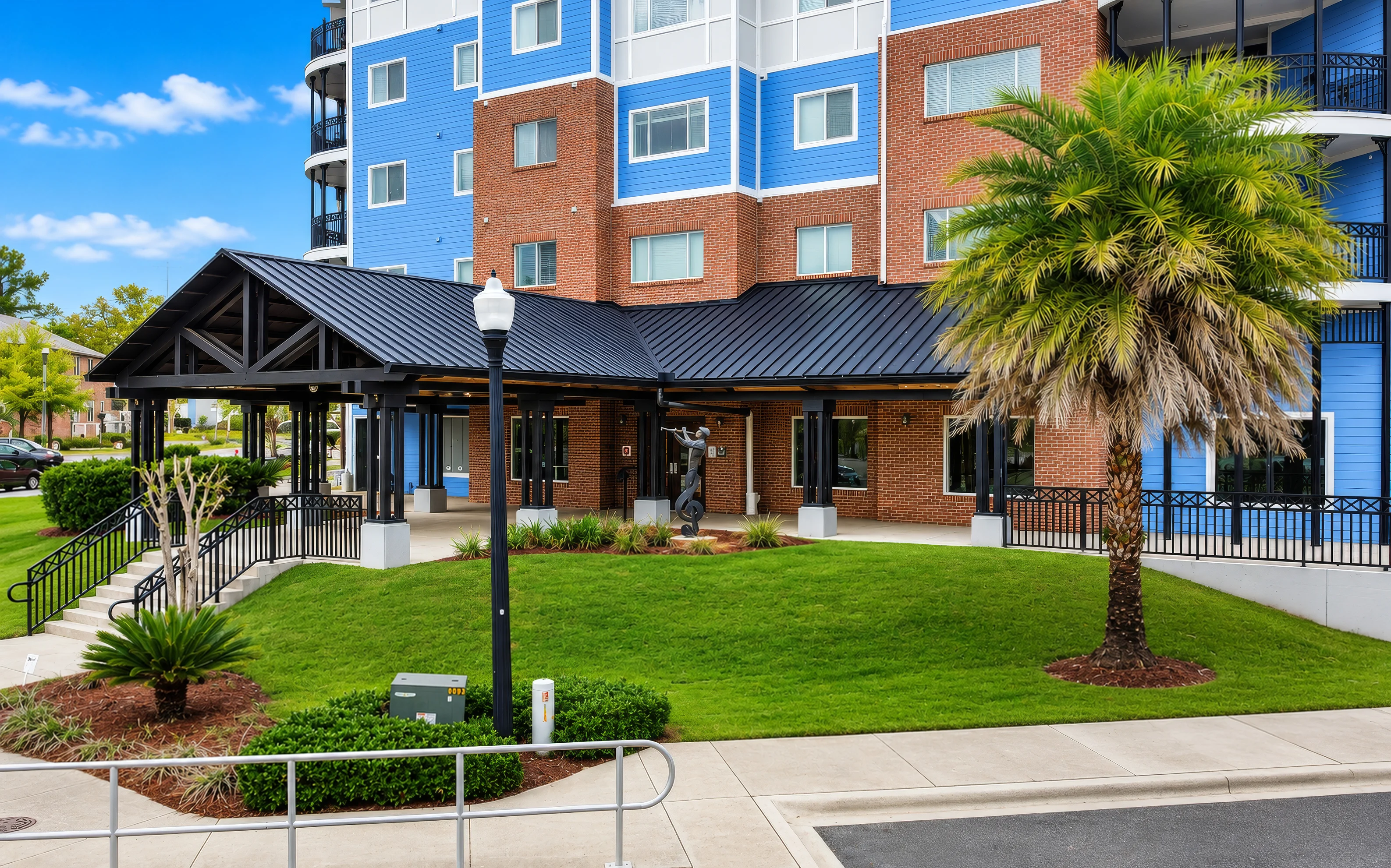 Exterior view of an apartment community entrance with a landscaped area and palm trees.