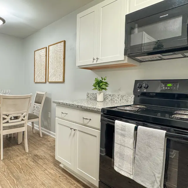 Modern kitchen featuring black appliances, white cabinetry, and a dining area with a wooden table and chairs.