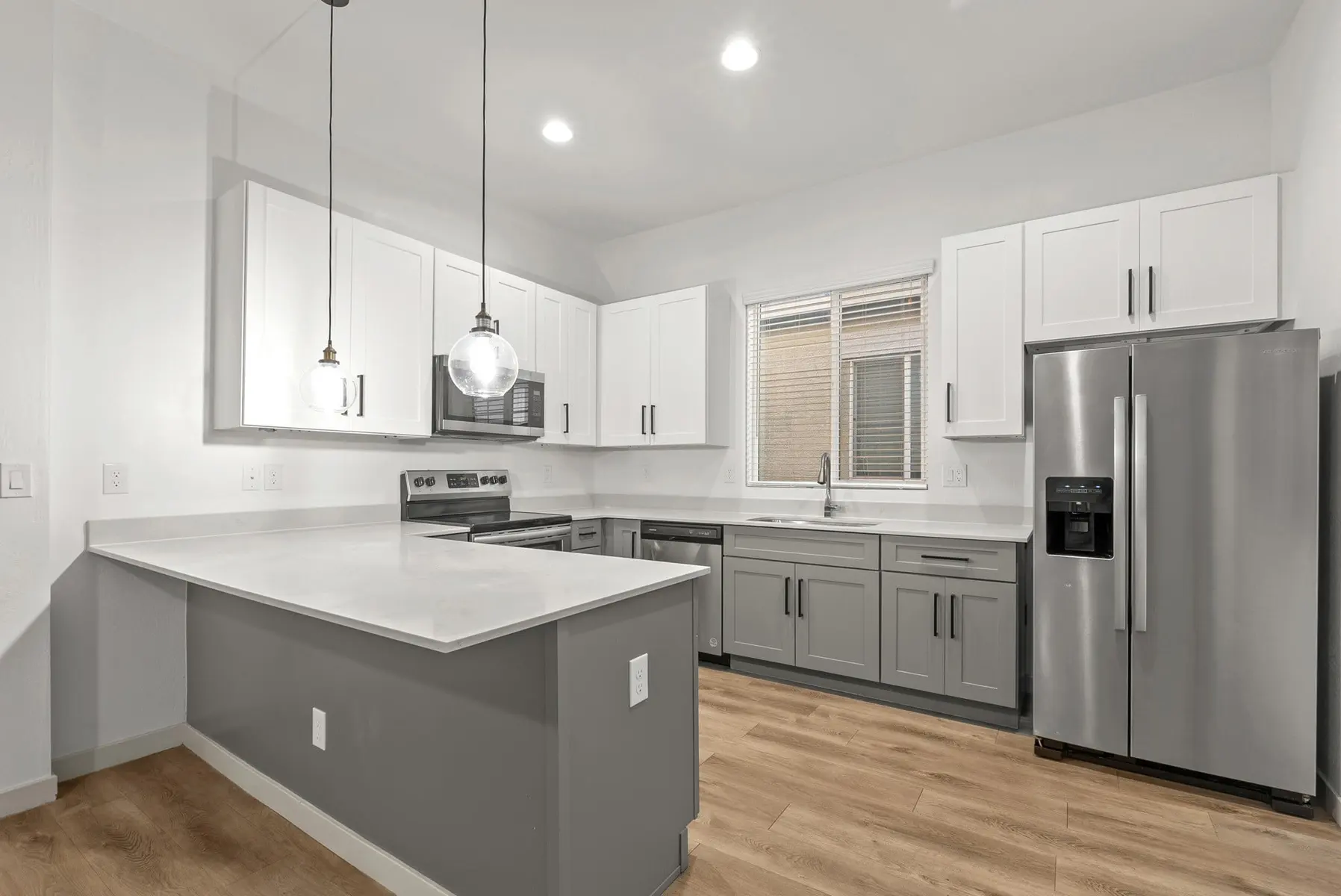 Modern kitchen with gray cabinets, white countertops, stainless steel appliances, and pendant lighting. Bright and spacious design.