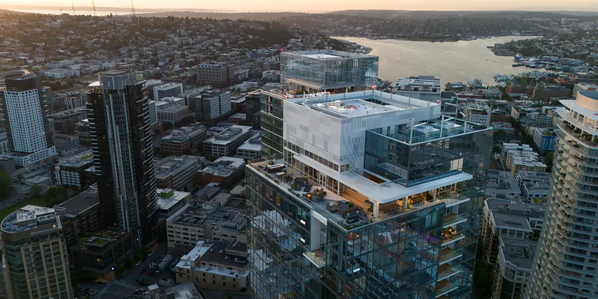 Aerial view of Seattle skyline featuring modern high-rise buildings with a setting sun in the background, overlooking a waterway.