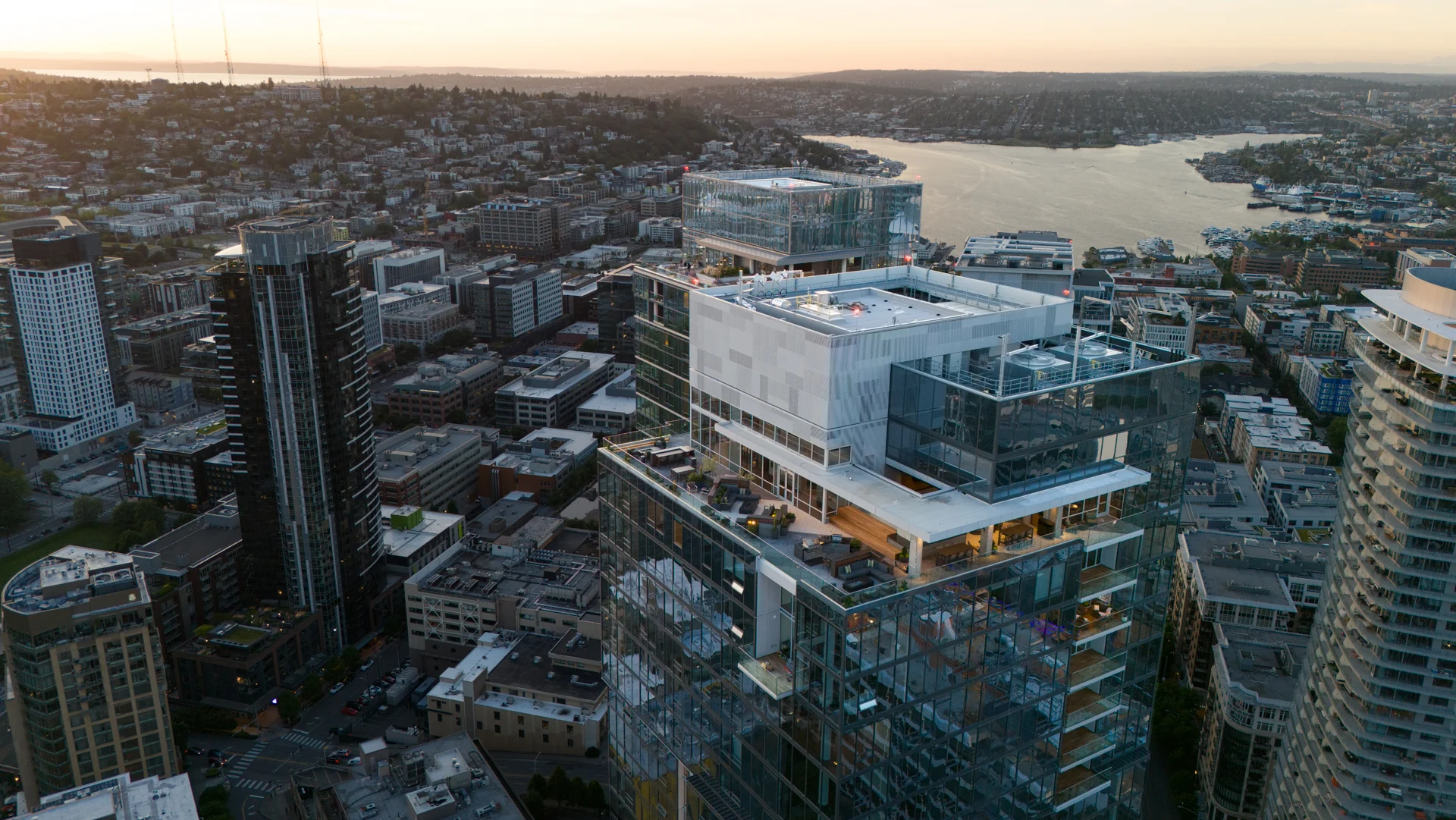 Aerial view of Seattle skyline featuring modern high-rise buildings with a setting sun in the background, overlooking a waterway.