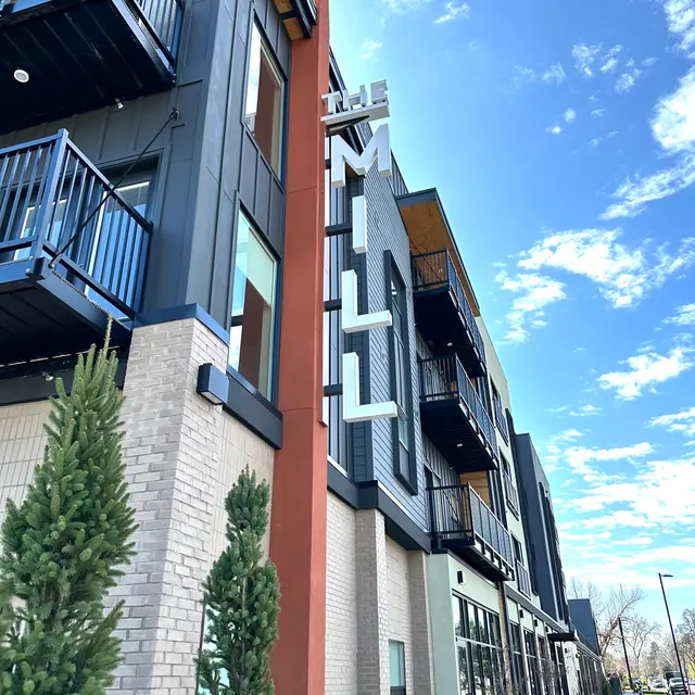 A modern building with a sign that reads 'The Mill', featuring balconies and a clear blue sky in the background.