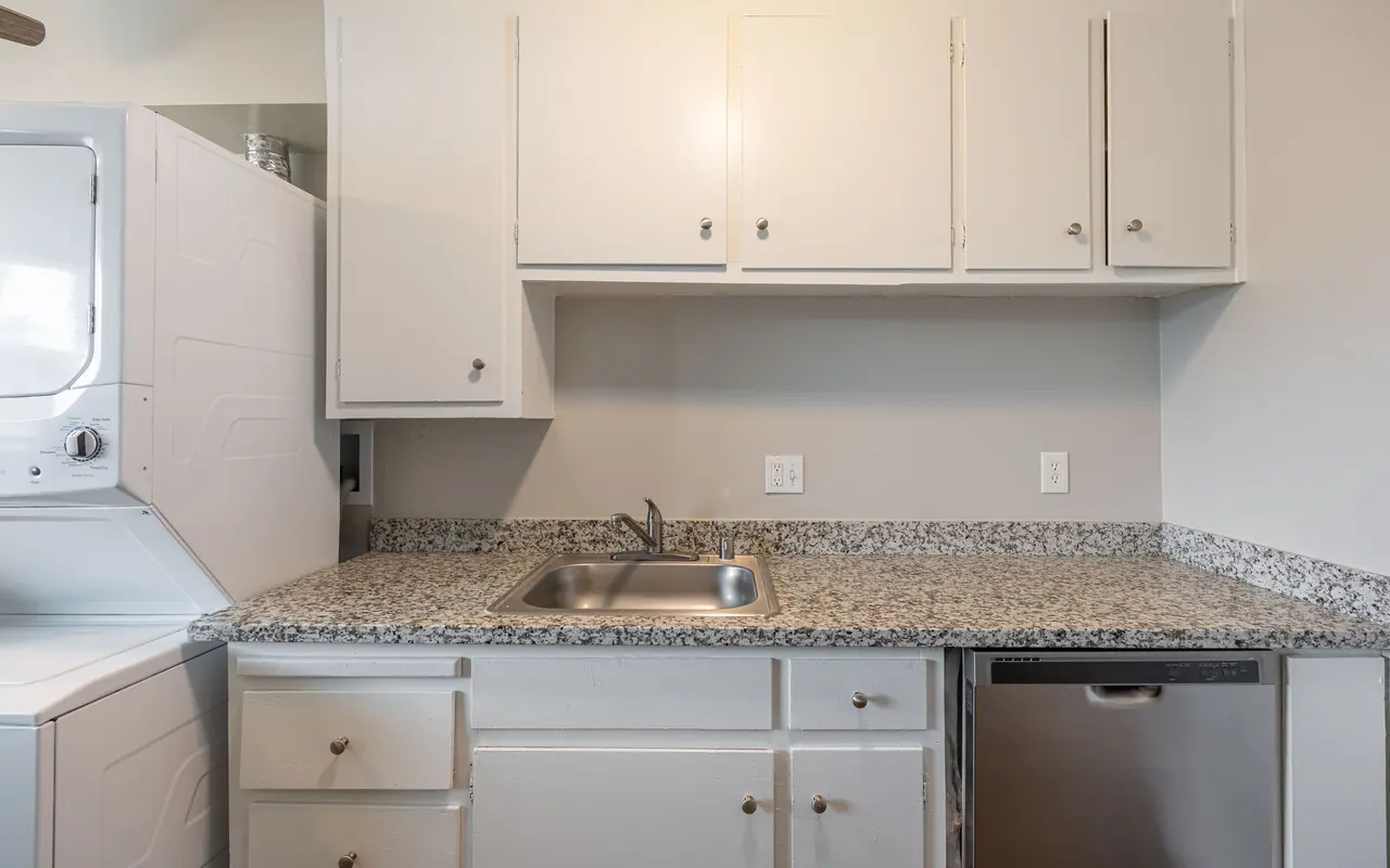 A modern kitchen with white cabinets, a granite countertop, and stainless steel appliances, including a dishwasher and a laundry unit.