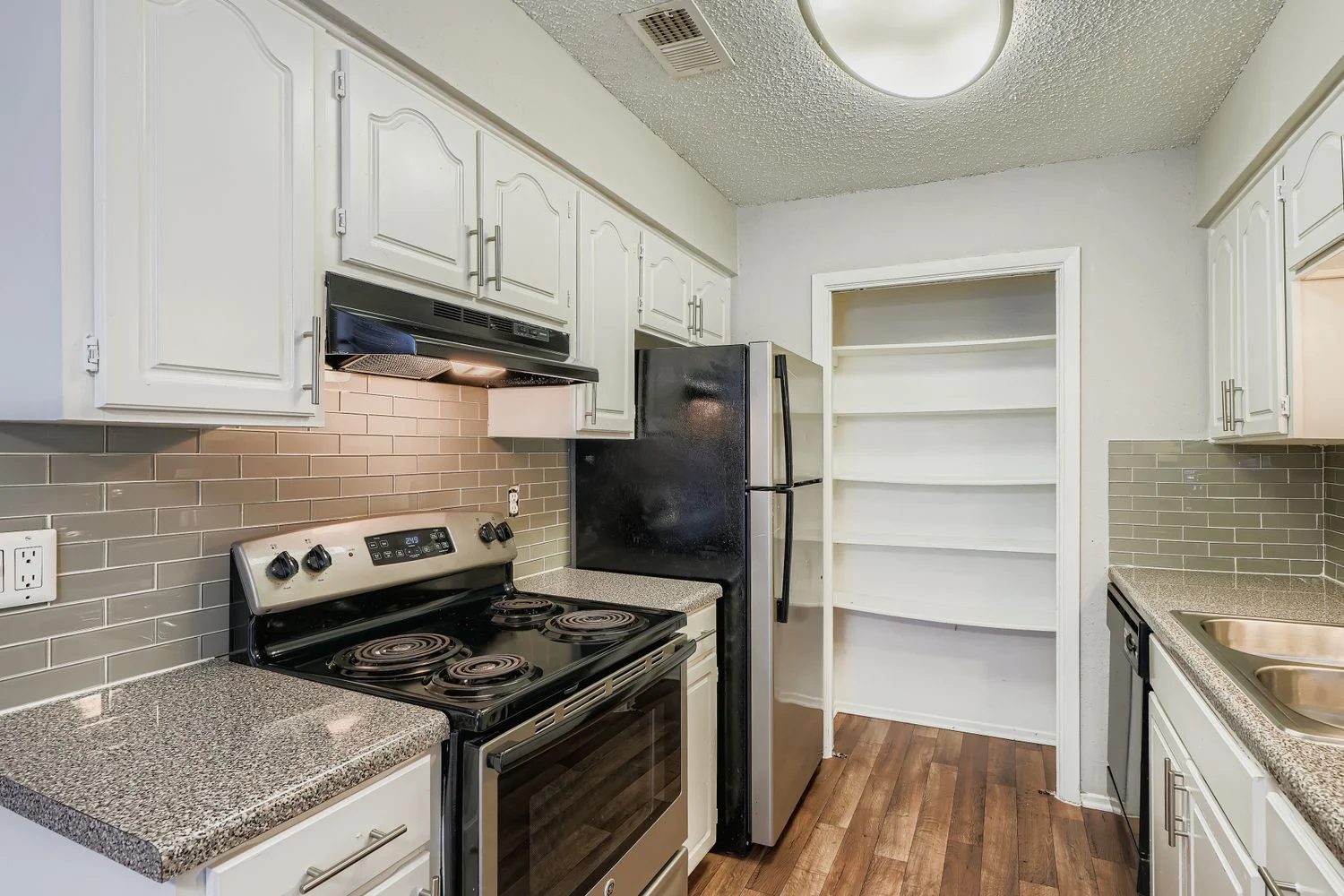 A modern kitchen featuring white cabinets, a black stove, and a refrigerator. The kitchen has a tiled backsplash and a pantry with open shelving.