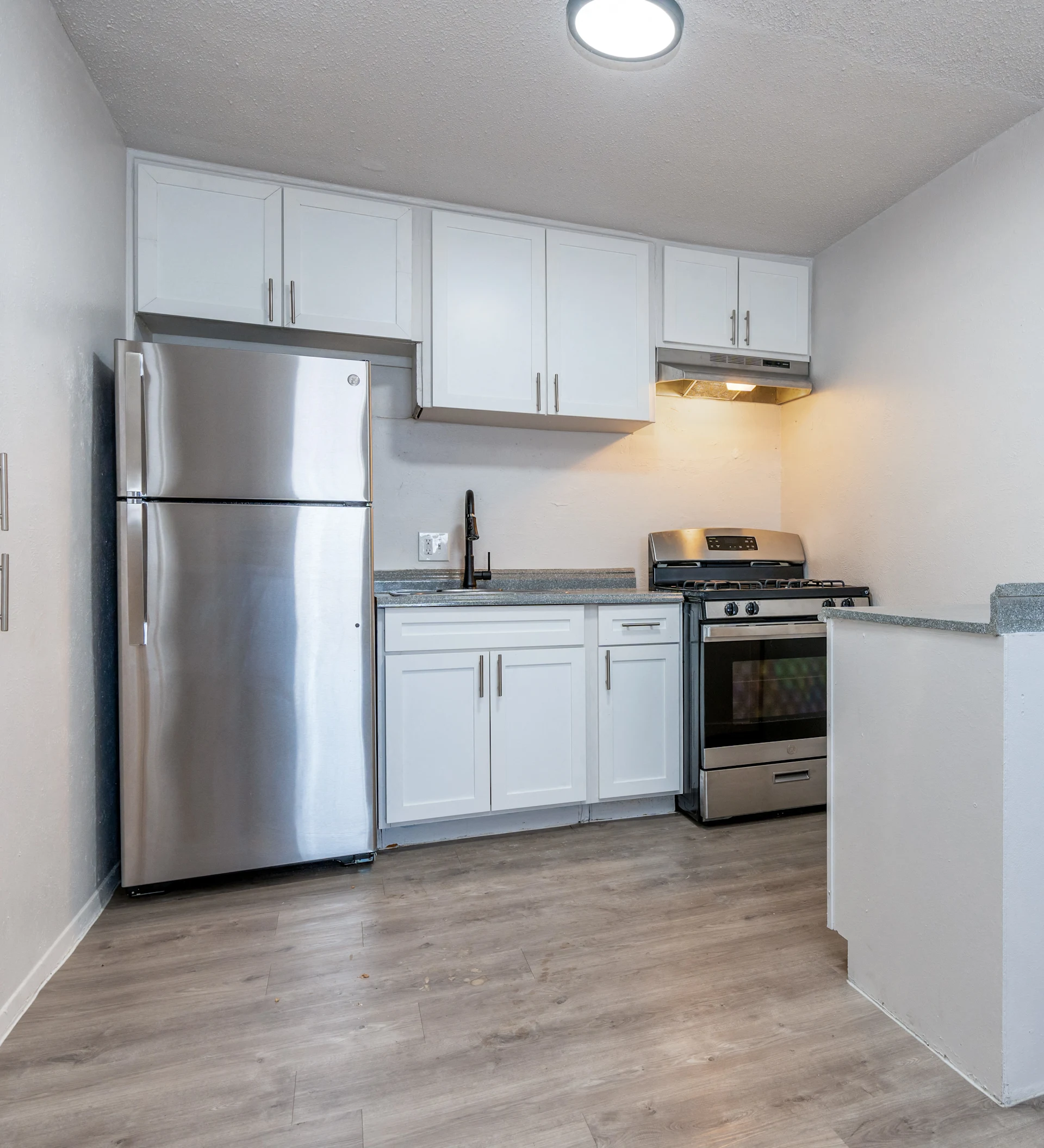 A modern kitchen featuring stainless steel appliances, including a refrigerator and a gas stove, along with white cabinetry and countertops.