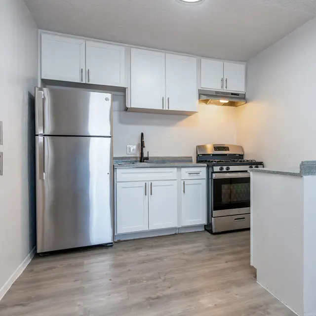 A modern kitchen featuring stainless steel appliances, including a refrigerator and a gas stove, along with white cabinetry and countertops.