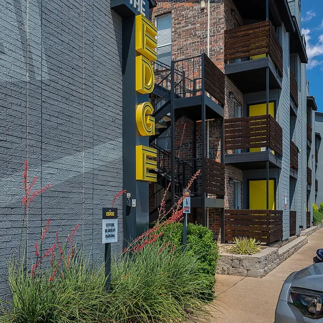 Exterior view of an apartment building named The Edge, featuring a modern design with wooden balconies and vibrant yellow accents.