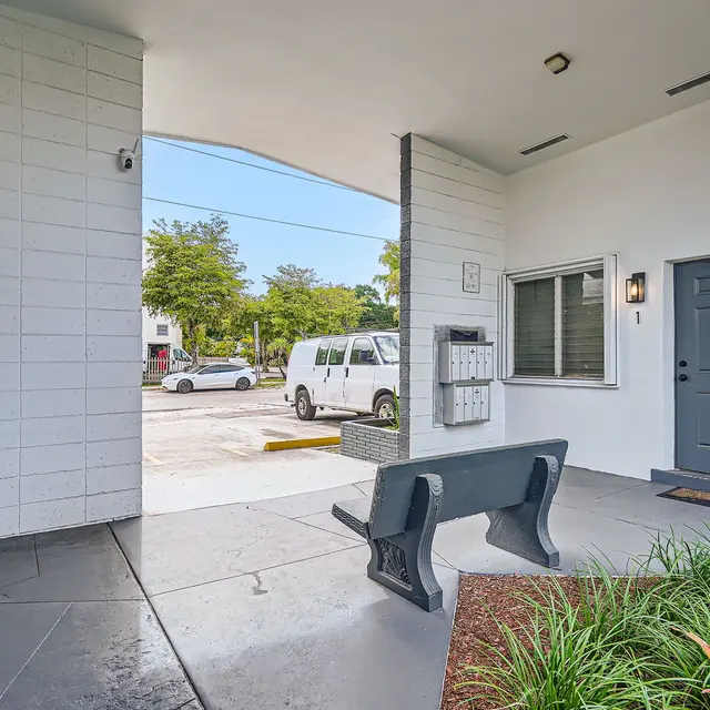 A view of the entrance area of a building, featuring a bench, a door, and mailboxes.