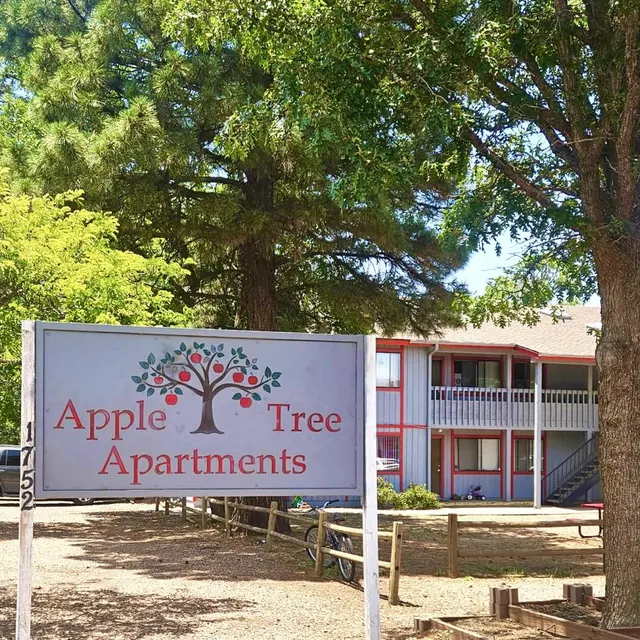 Apple Tree Apartments Signage A sign for Apple Tree Apartments with a tree design in the background and an apartment building visible in the distance.
