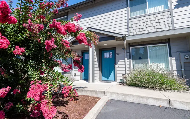 Exterior view of a building with blue doors and pink flowering plants in front.