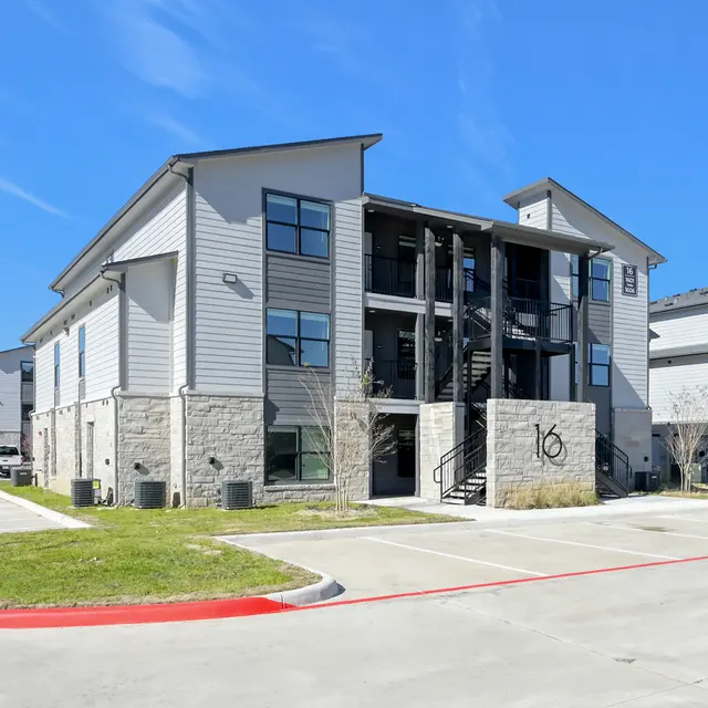 A view of a modern apartment building featuring a mix of stone and siding exterior with multiple windows and balcony access.
