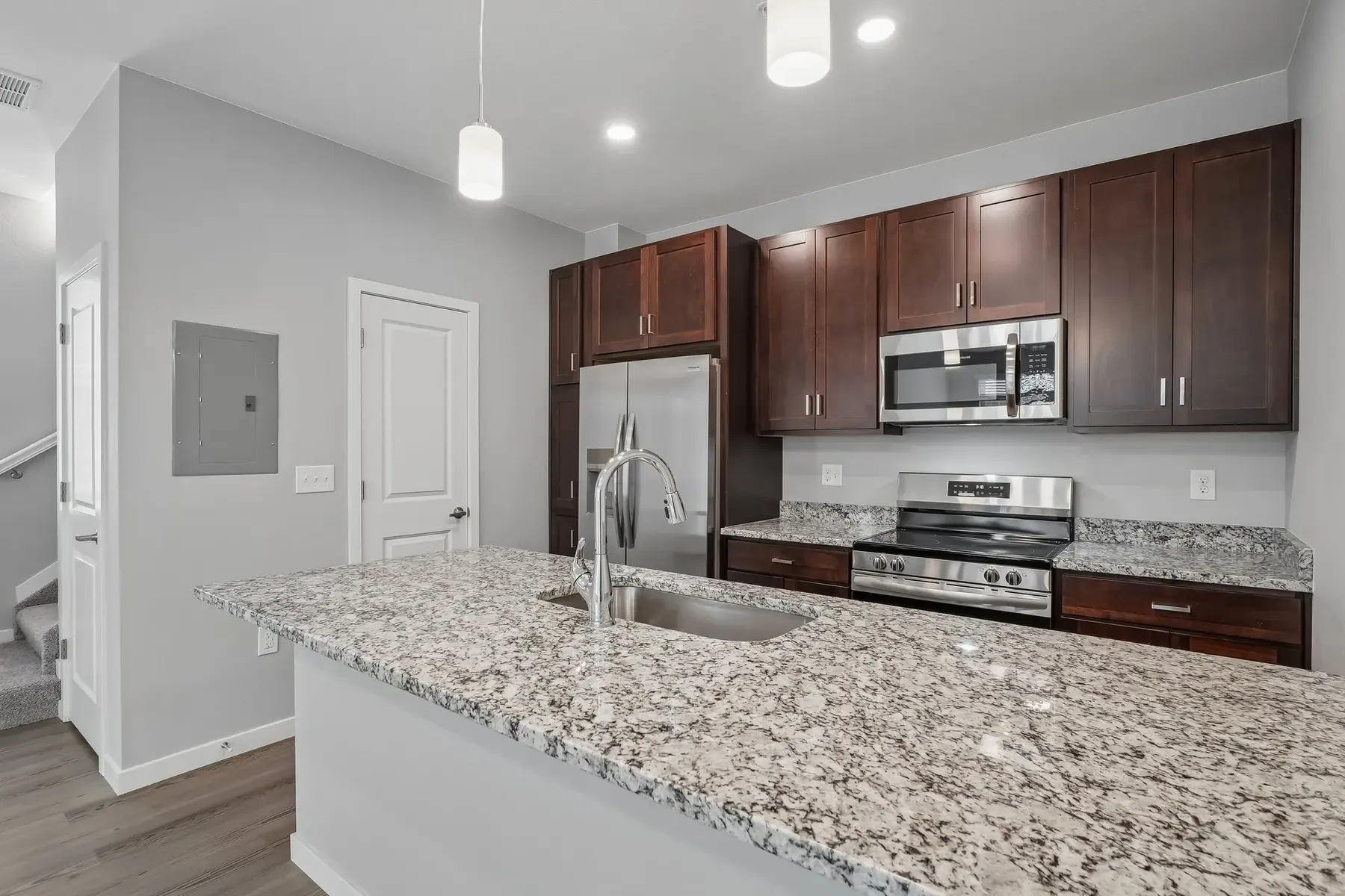 A modern kitchen featuring dark wood cabinets, stainless steel appliances, and a granite countertop with a sink.