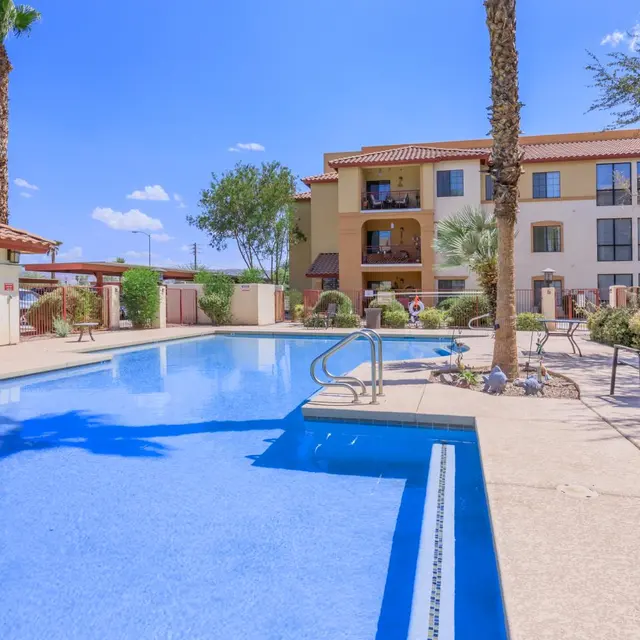 Swimming Pool at Apartment Complex A clear blue swimming pool surrounded by a sunny courtyard with palm trees and an apartment building in the background.