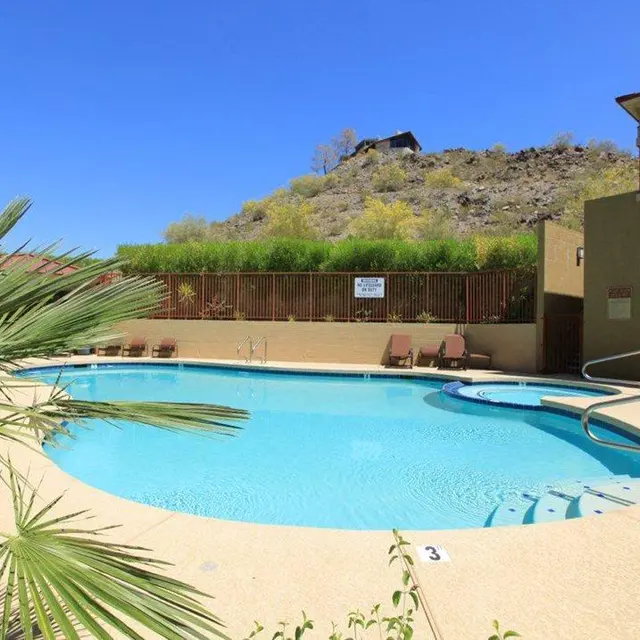 Relaxing Poolside Retreat A clear swimming pool surrounded by lounge chairs and tall green plants, with a mountain in the background under a bright blue sky.
