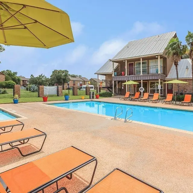 A sunny outdoor swimming pool area with lounge chairs and umbrellas