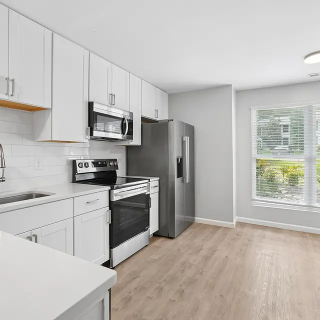 Modern kitchen featuring white cabinets, stainless steel appliances, and a large window letting in natural light.