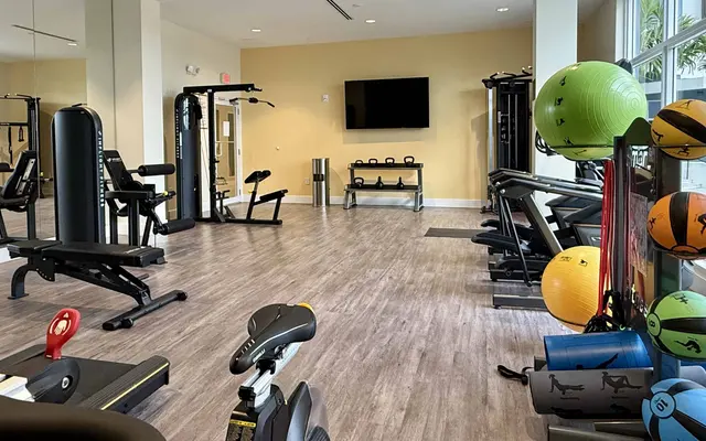 Modern gym interior with various fitness equipment including weights, exercise bikes, and medicine balls.