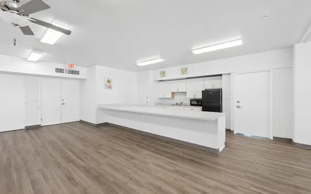 Spacious and modern kitchen and living area with wood flooring, white walls, and appliances