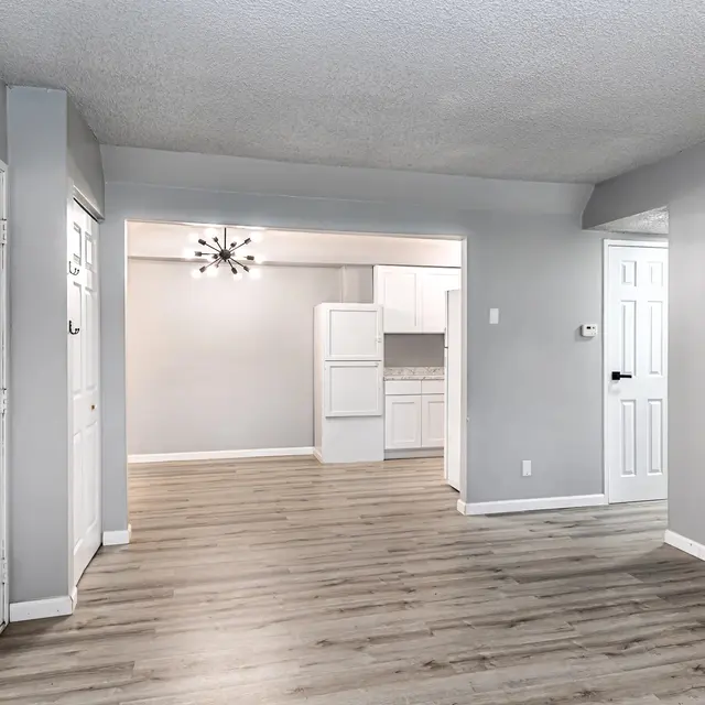 View of a modern apartment living room with a light fixture, light gray walls, and wood-like flooring.