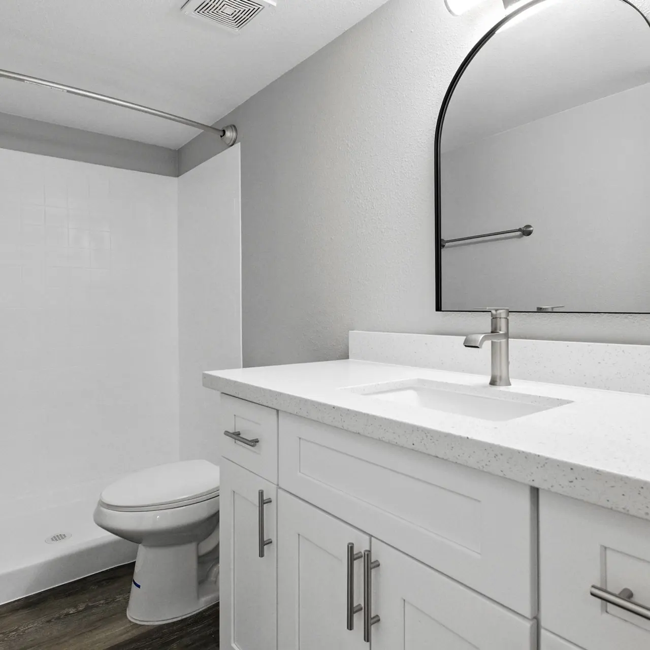 Modern Bathroom Design A modern bathroom featuring a white countertop with a rectangular sink, a large round mirror, and a clean shower area to the left. The wall is painted light grey and the floor has wooden tiles.