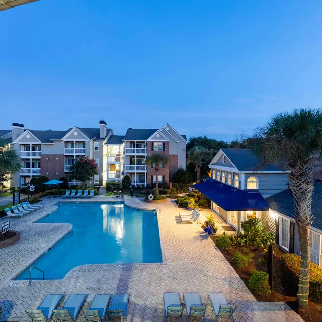 View of a pool area in an apartment complex during twilight, featuring seating around the pool and palm trees.