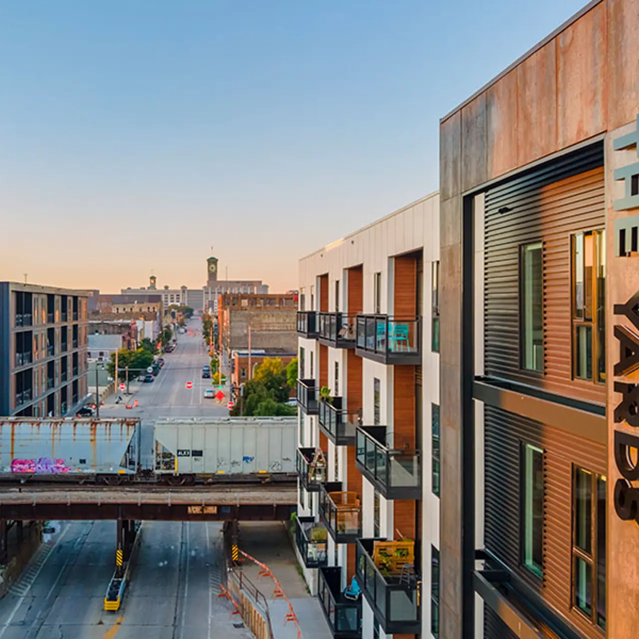 Aerial view of The Yards apartment complex A modern apartment complex named 'The Yards' overlooking a city street with buildings, a train track, and distant structures under a clear blue sky.