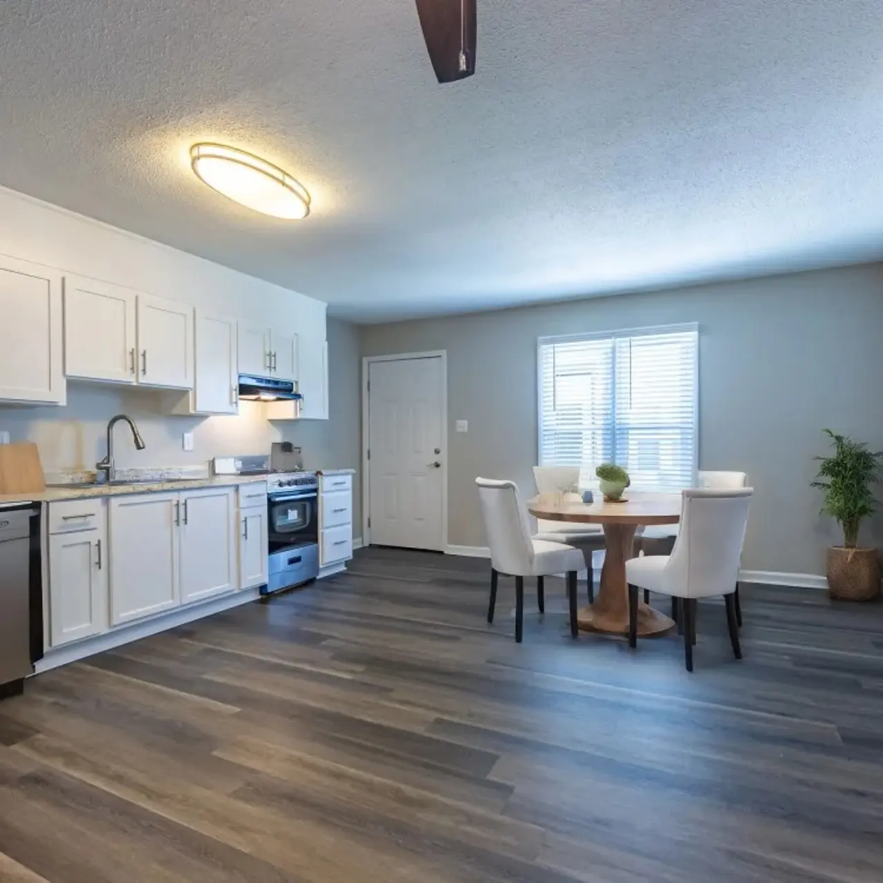 A modern kitchen with white cabinets, stainless steel appliances, and hardwood flooring. A round dining table with four chairs is situated near a window.