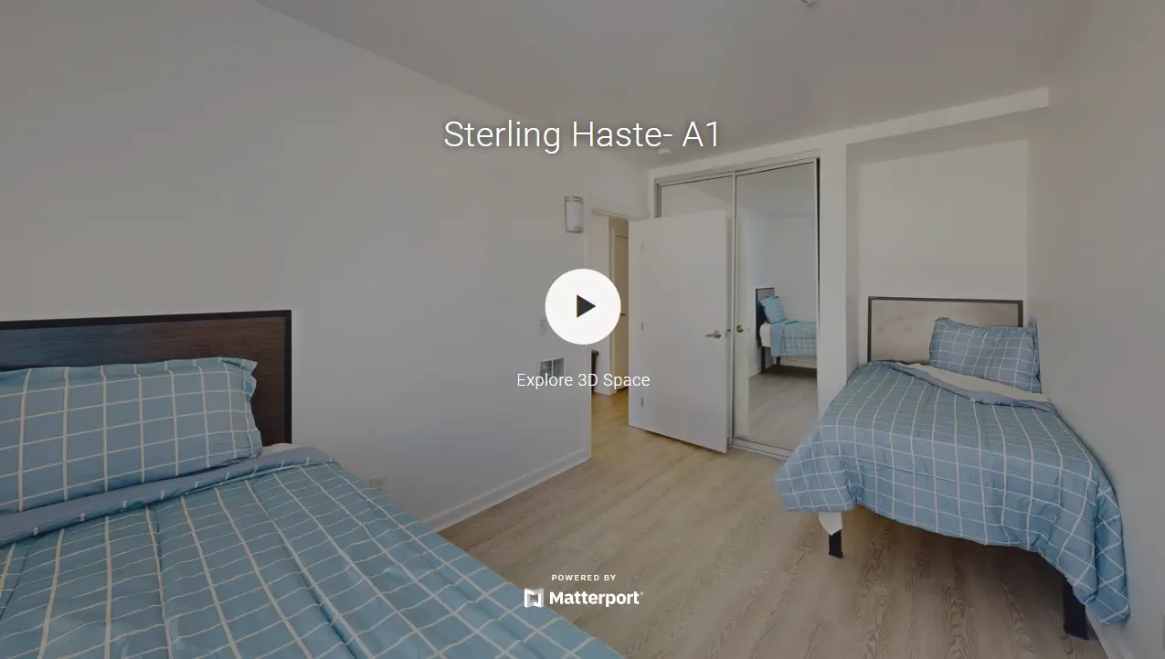 A spacious bedroom featuring two twin beds with blue checkered bedding, light wooden flooring, and a closet door in the background.