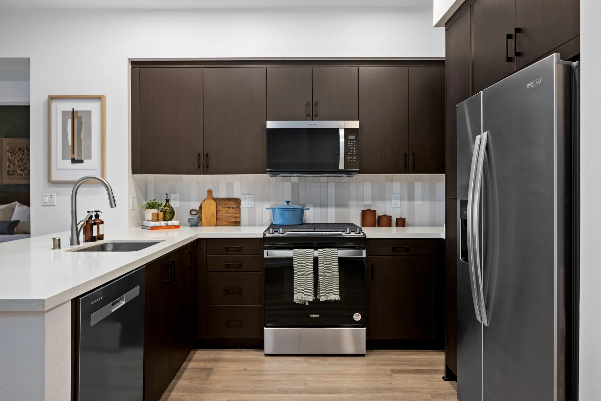 Modern Kitchen Interior A modern kitchen featuring dark cabinets, stainless steel appliances, and a white countertop with a sink. Baking utensils and a blue pot are visible on the countertop.