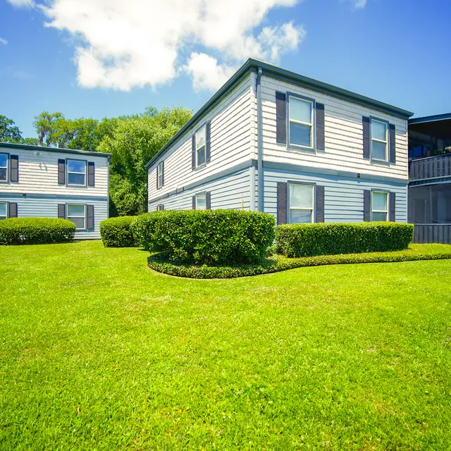 Exterior view of a two-story apartment complex surrounded by green grass and hedges under a blue sky.