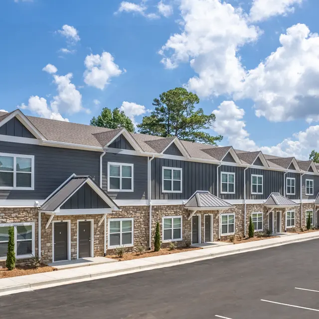 A row of townhouse-style buildings with stone and siding exteriors under a clear blue sky.