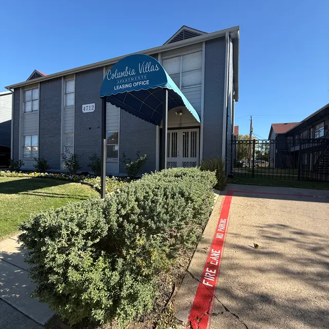 Exterior view of a leasing office at Columbia Villas, with a blue awning and landscaped greenery.