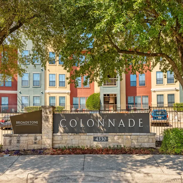 Exterior view of the Colonnade apartments with a stone sign and landscaped trees.
